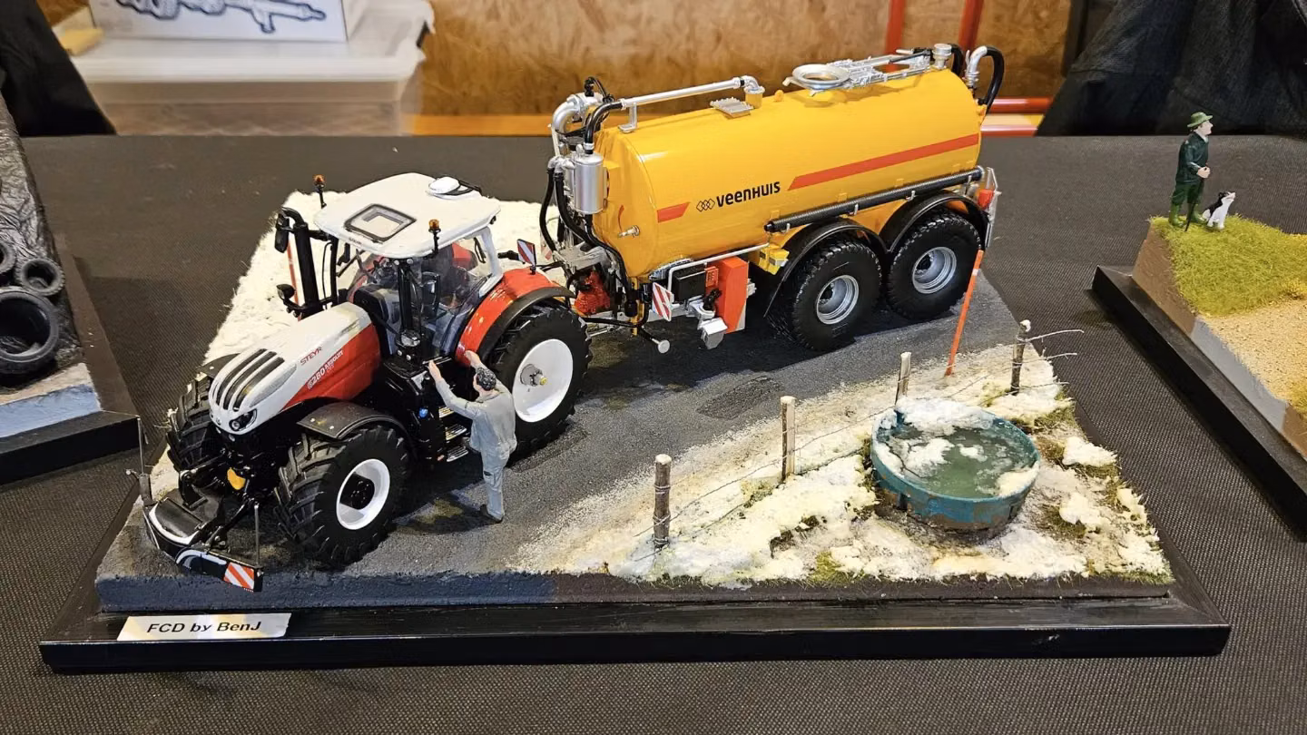 A model tractor with a front weight bumper is displayed on a diorama with a tank trailer and farm figures