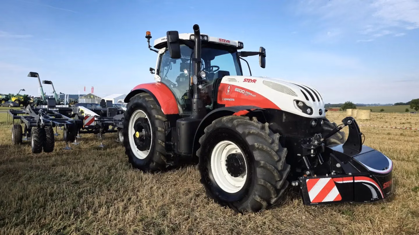 Tractor with a large front weight bumper featuring red and white reflective stripes, parked on a grassy field