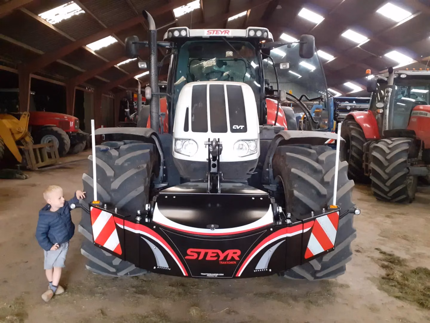 A Steyr tractor with a front weight bumper featuring red and white safety stripes and LED lights in a barn