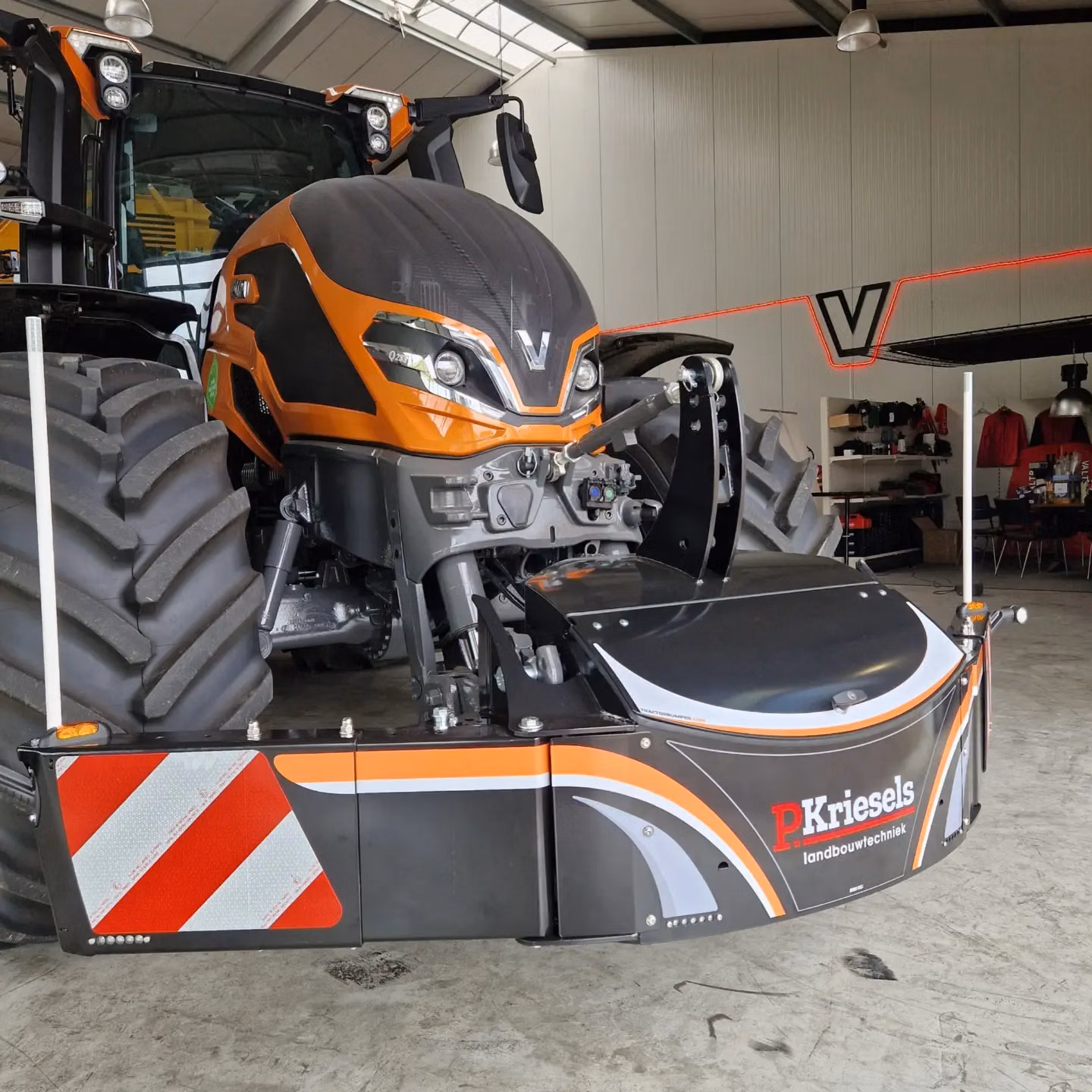 Orange tractor indoors with a large front weight bumper featuring reflective stripes and "P. Kriesels landbouwtechniek" text