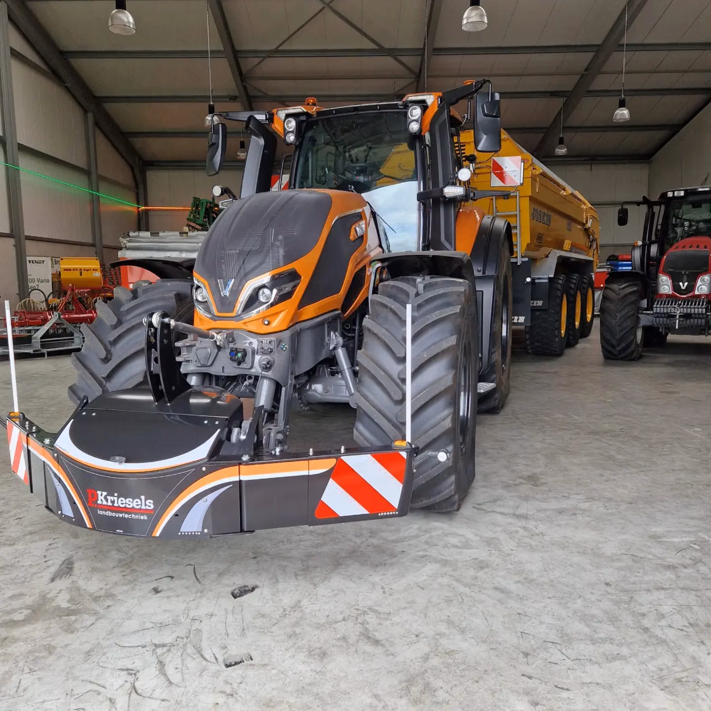 A large orange tractor with a mounted front weight bumper featuring red and white warning stripes indoors