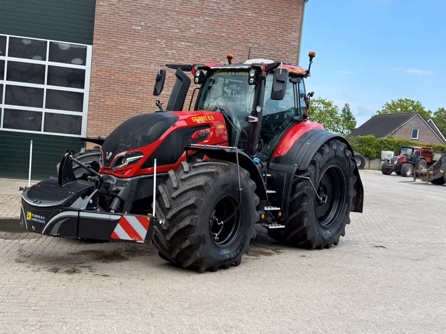 A red tractor fitted with a black front weight bumper featuring LED lights, reflective strips and storage compartment.
