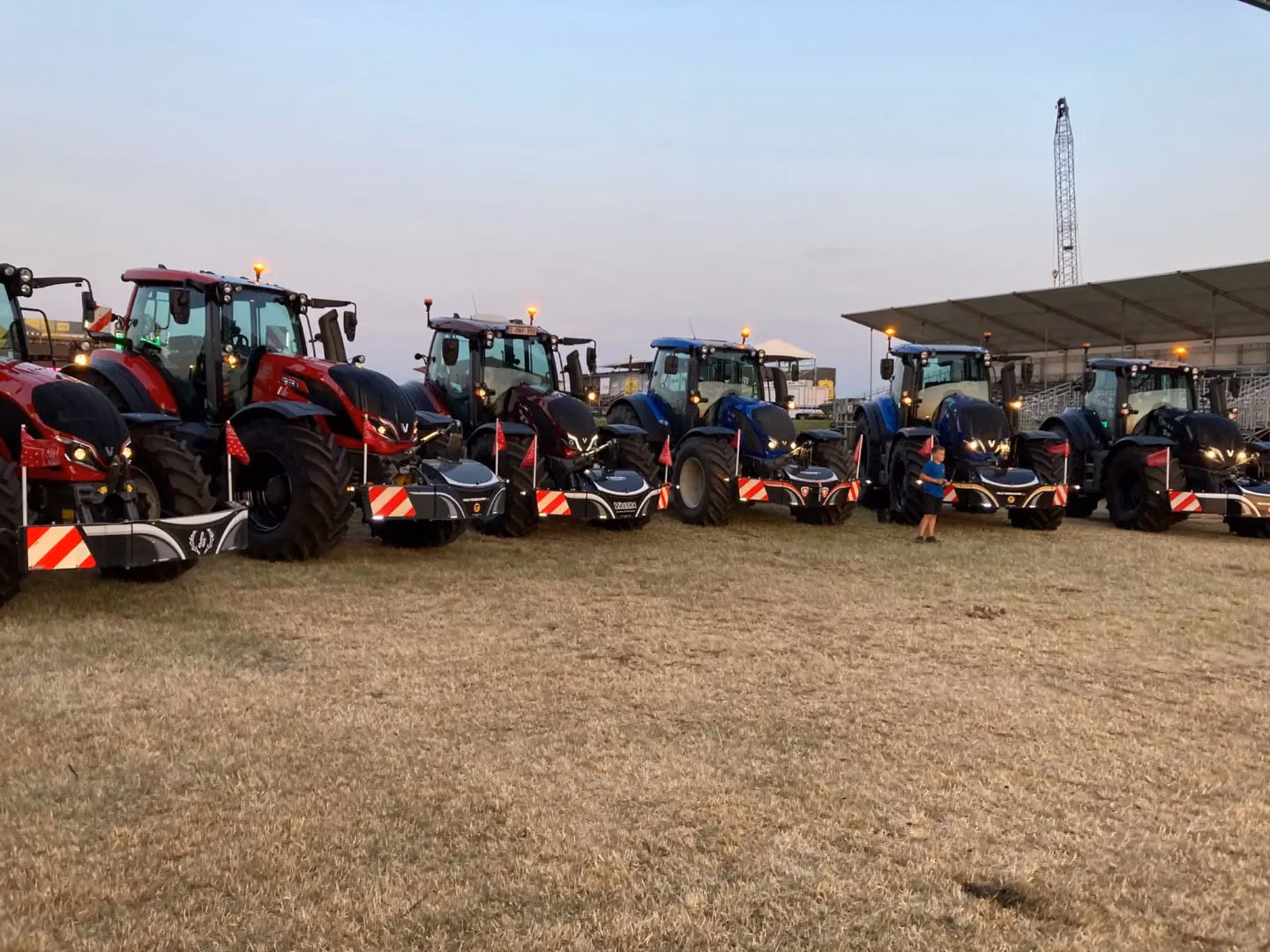 A row of red and blue tractors on grass, each equipped with front weight bumpers featuring safety LED lights