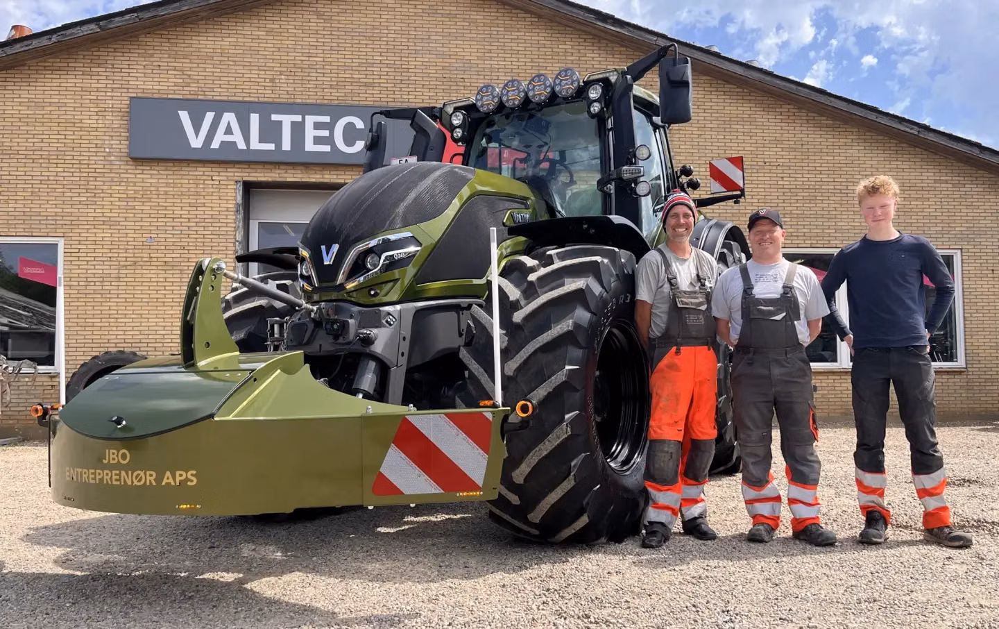 Three people standing beside a large tractor with a green front weight bumper marked JBO ENTREPRENØR APS