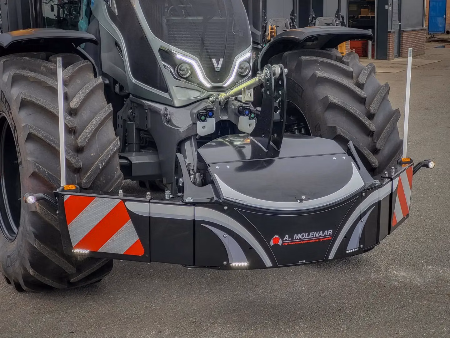 Front view of a tractor with a large black front weight bumper featuring LED lights and reflective red-white panels
