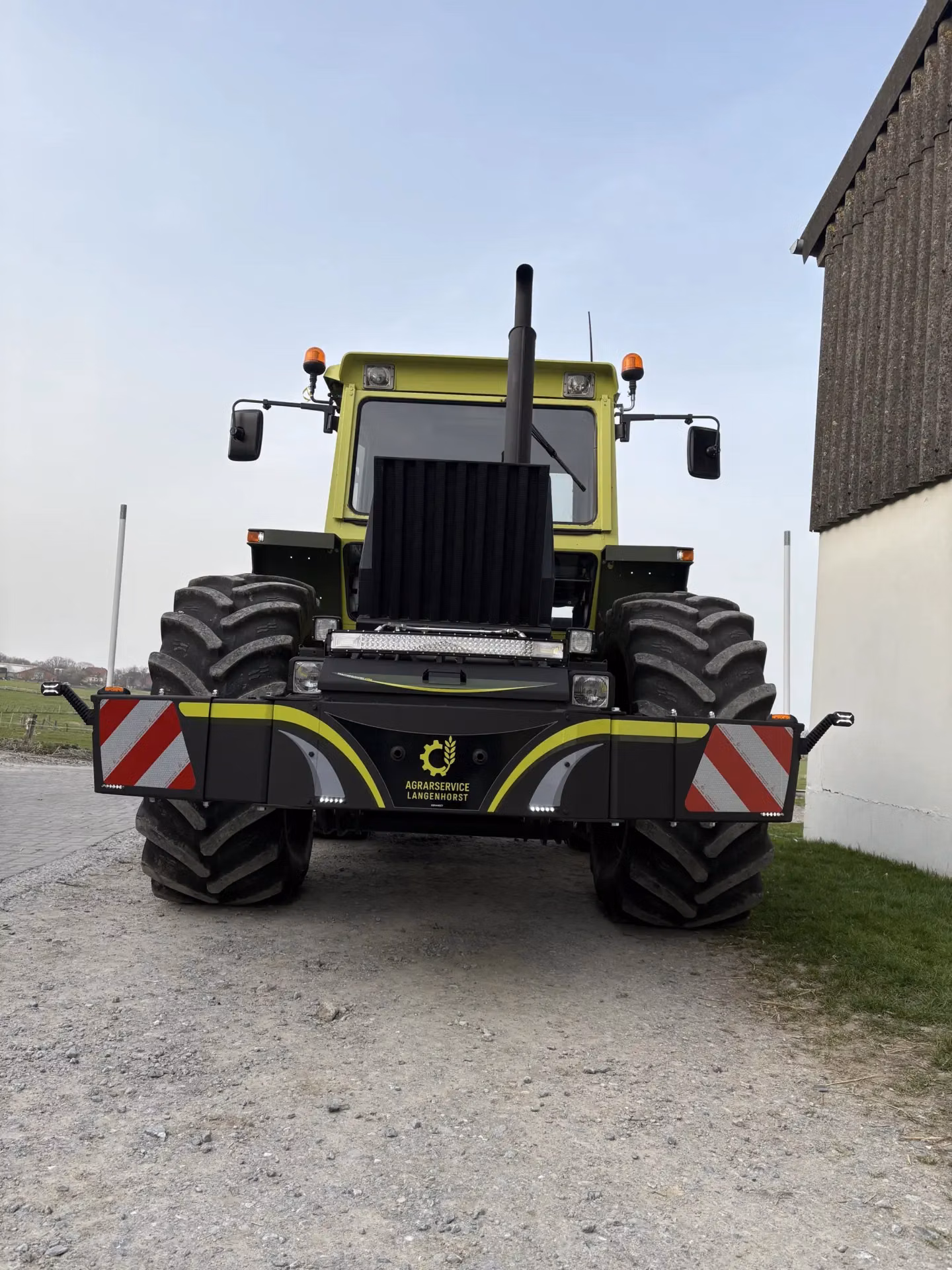 Large green tractor with a black front weight bumper featuring reflective red and white stripes and LED lights
