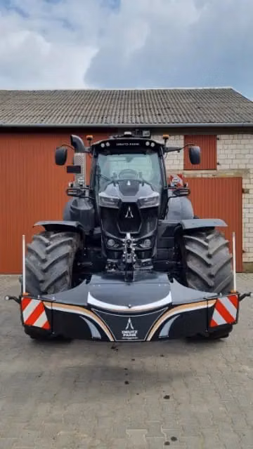 A large tractor with a mounted front weight bumper featuring reflective stripes, parked on a paved surface.