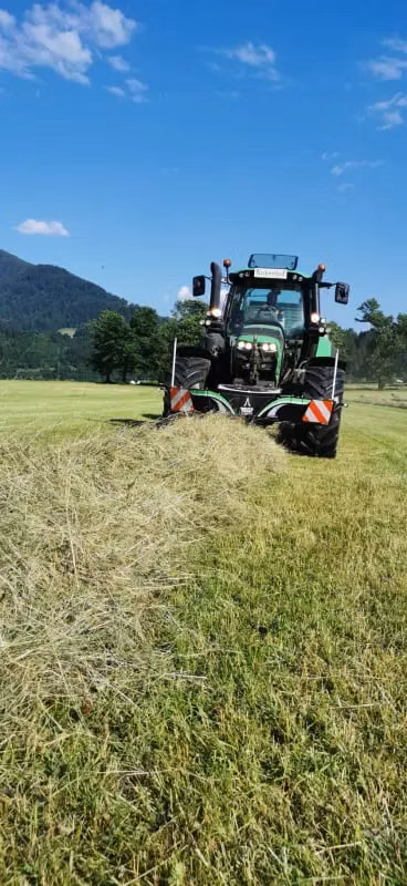 A green tractor with a front weight bumper and LED lights works in a grassy field on a clear sunny day