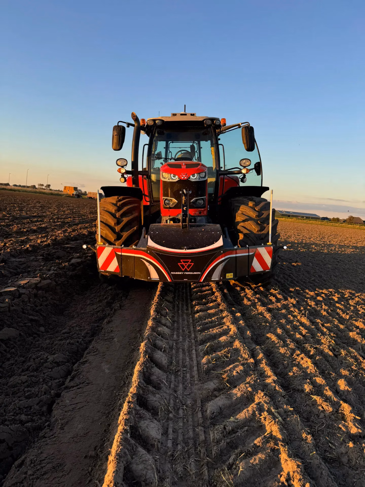 Red tractor with a Massey Ferguson front weight bumper parked on a plowed field at sunset