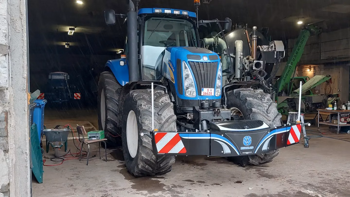 Blue tractor equipped with a front weight bumper featuring reflective red and white stripes in a workshop