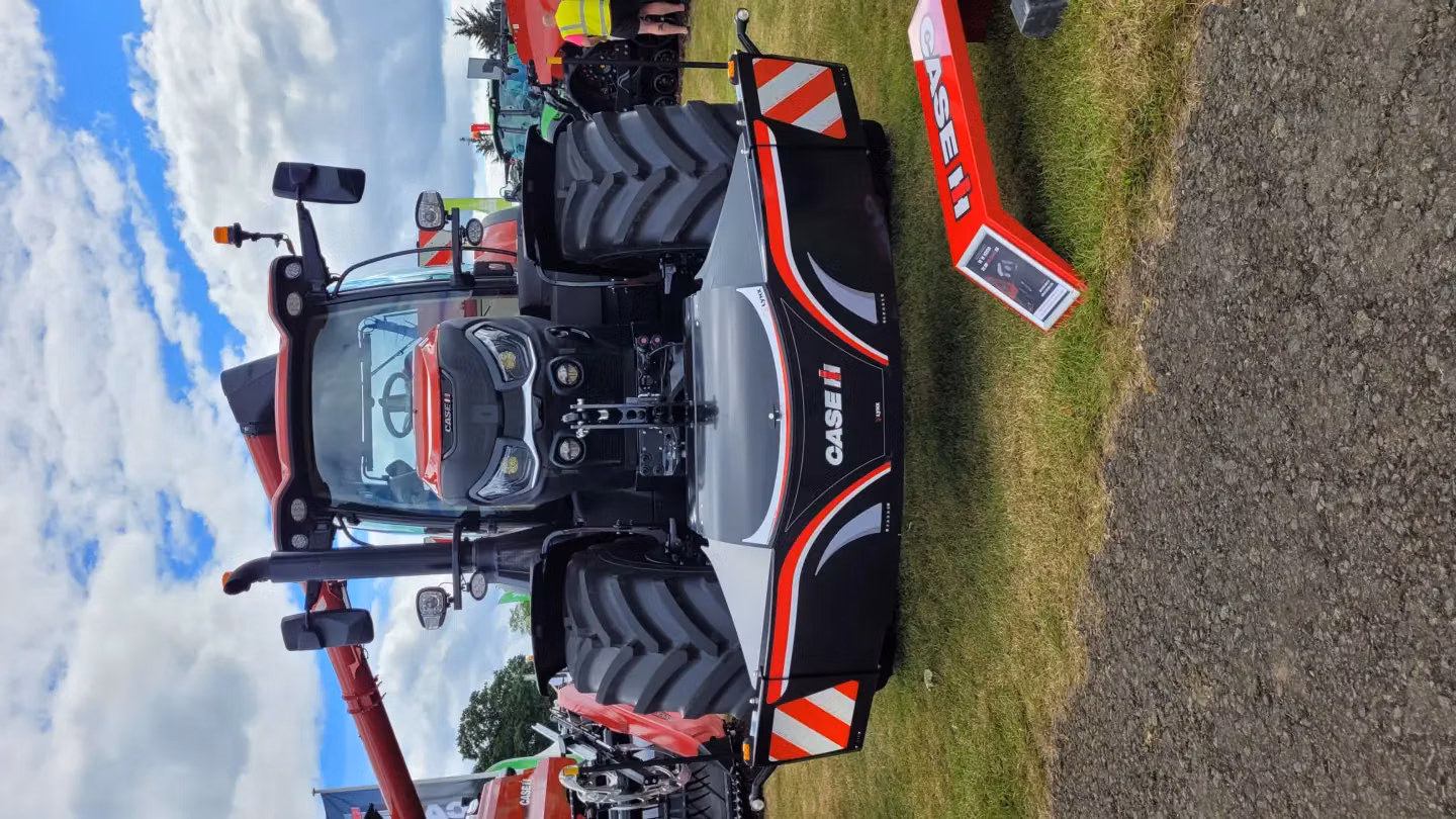 A Case IH tractor fitted with a large black front weight bumper featuring red and white accents on grass.