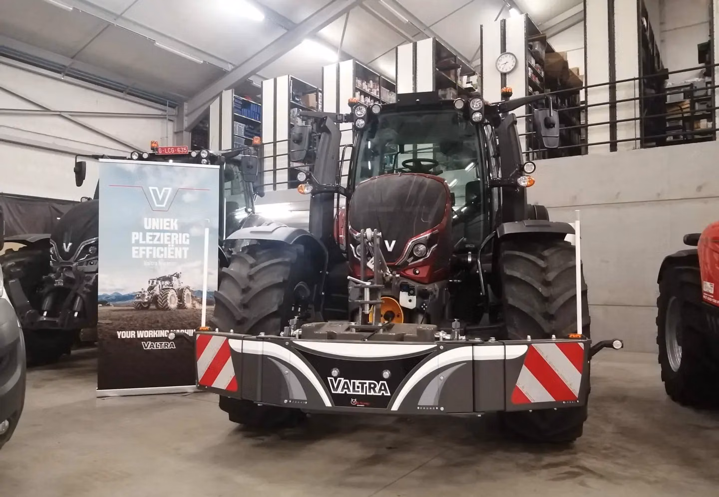 A tractor in a showroom fitted with a Valtra-branded front weight bumper featuring reflective stripes