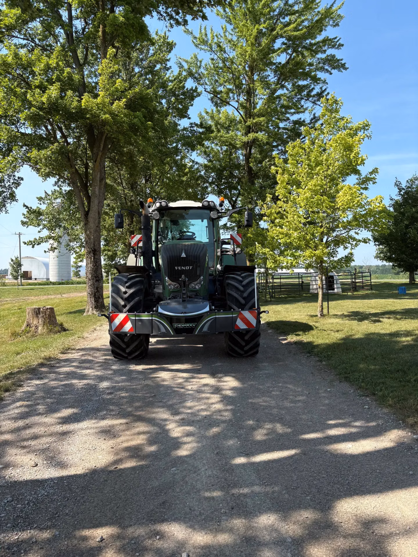 A tractor with a front weight bumper is parked on a dirt path between green trees on a sunny day