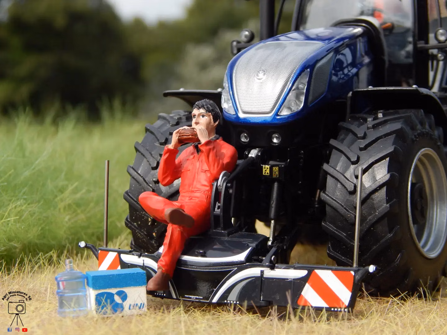 A model tractor with a front weight bumper and warning stripes, with a figurine in red overalls sitting and eating
