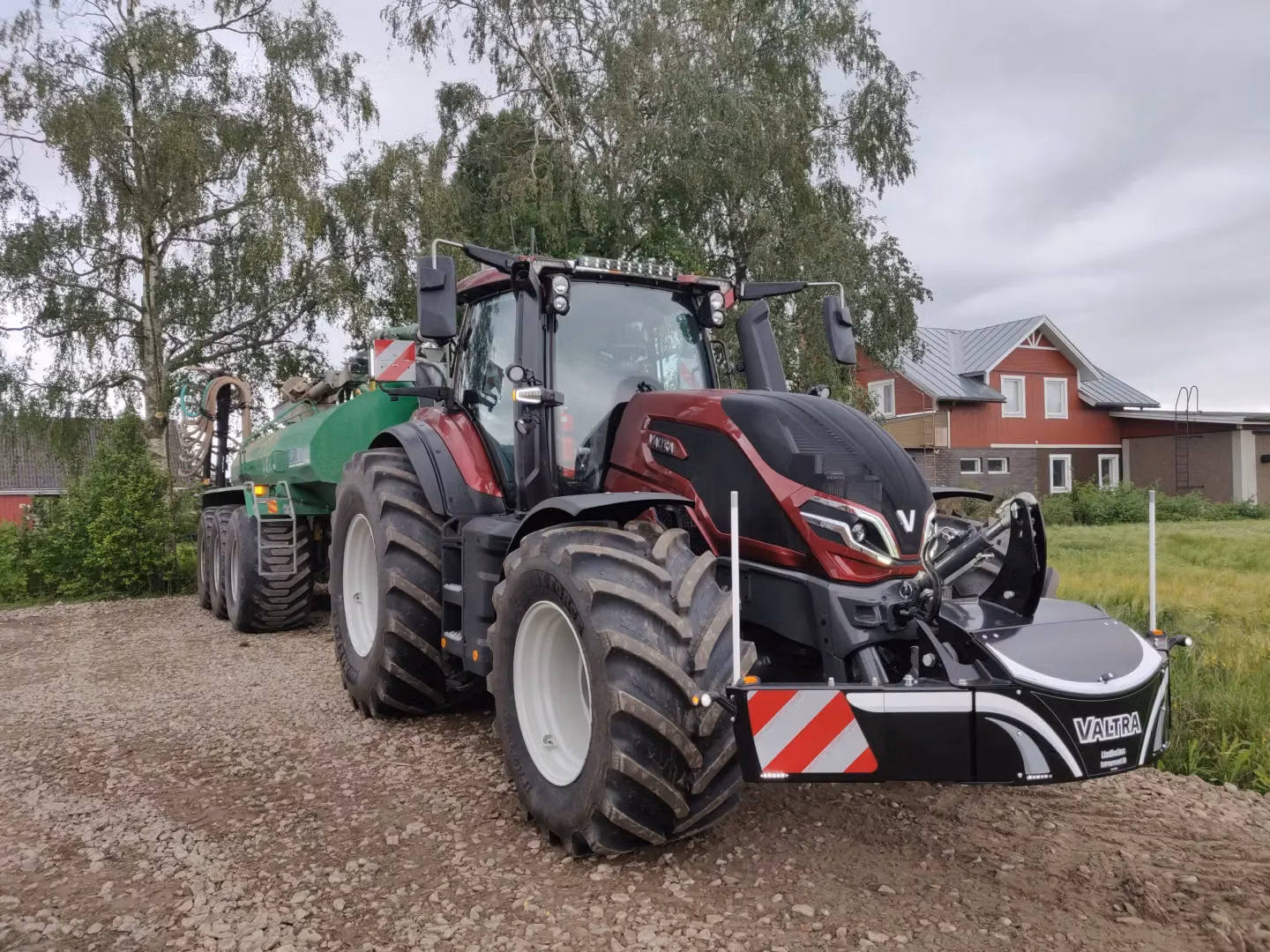 A large tractor with a front weight bumper featuring safety stripes, LED lights and Valtra branding on a farm road