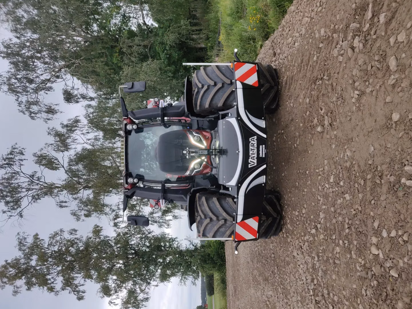 A tractor on a dirt path fitted with a front box bumper featuring reflective stripes and LED lights