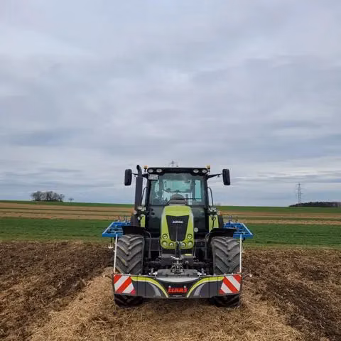 A tractor fitted with a front weight bumper is parked on a dirt field under a cloudy sky