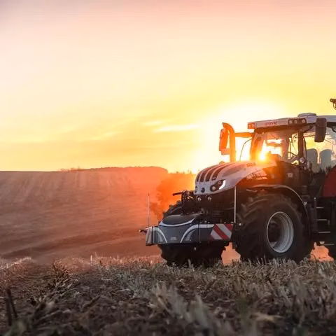 Tractor with a front weight bumper attached, parked in a harvested field at sunset