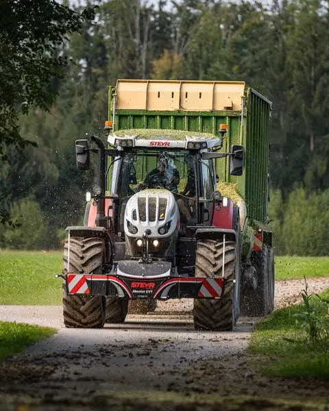 A tractor with a front weight bumper attached, pulling a loaded green trailer along a rural path