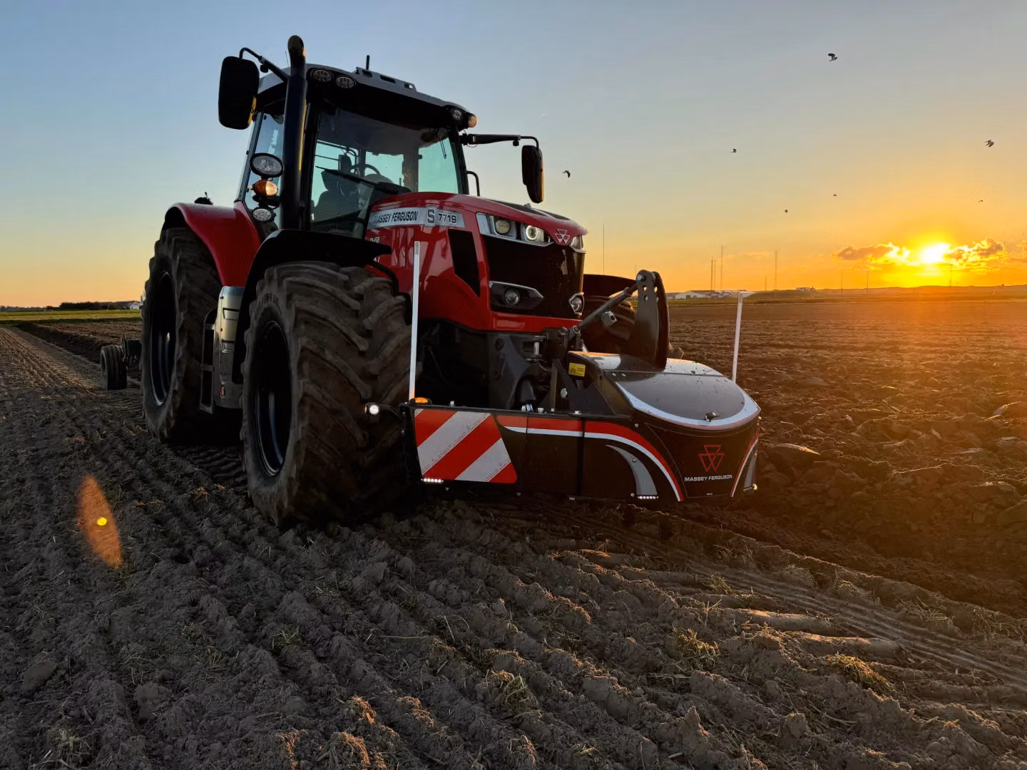 A red tractor with a front weight bumper attached is parked on a plowed field at sunset