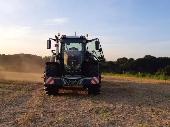 A tractor in a field with a front weight bumper attached, photographed from the front at sunset
