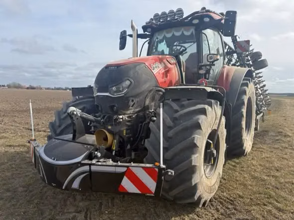 A large red tractor fitted with a front weight bumper and hazard markings is parked on a field