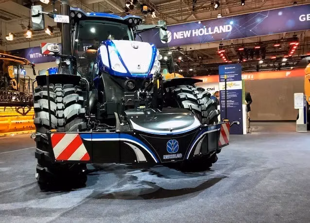 Large blue tractor with a front weight bumper featuring reflective red and white panels and integrated lights