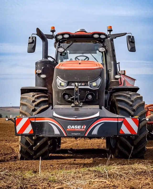 A red tractor with large tires is fitted with a CASE IH branded front weight bumper in a tilled field
