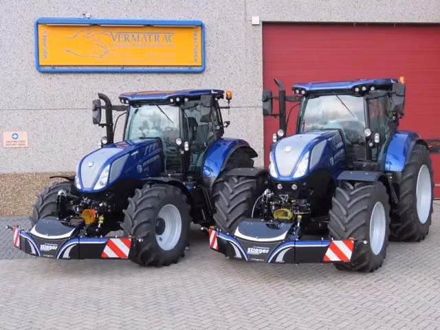 Two blue tractors parked side by side, each fitted with a large black front weight bumper with reflective stripes