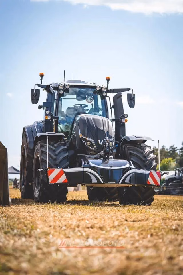 Black tractor with a front weight bumper featuring red and white reflective panels parked on dry grass