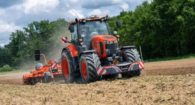 A tractor with a striped front weight bumper is working on a field, pulling agricultural equipment
