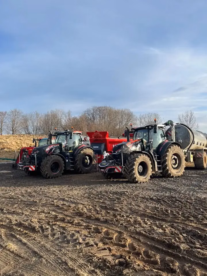 Two tractors with front weight bumpers attached are parked on muddy ground next to other farm equipment