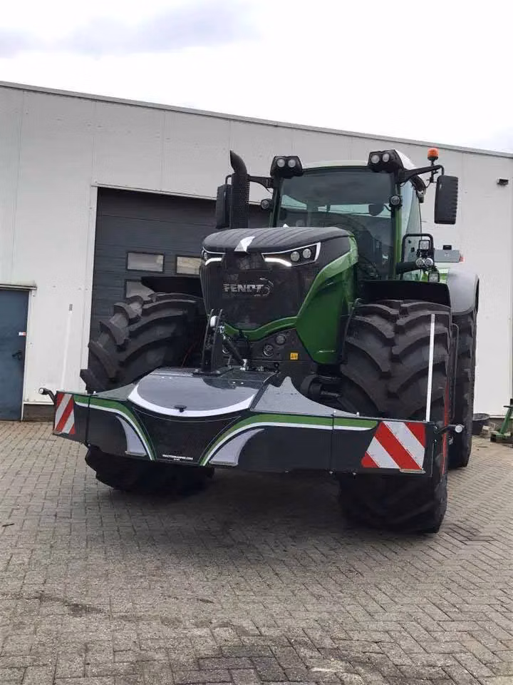 A green tractor fitted with a large front weight bumper featuring reflective red and white warning stripes