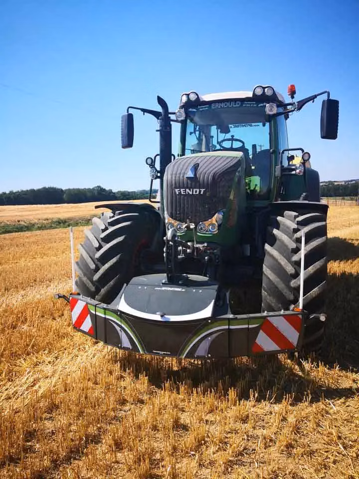 A tractor with a front weight bumper featuring reflective red and white stripes parked in a harvested field