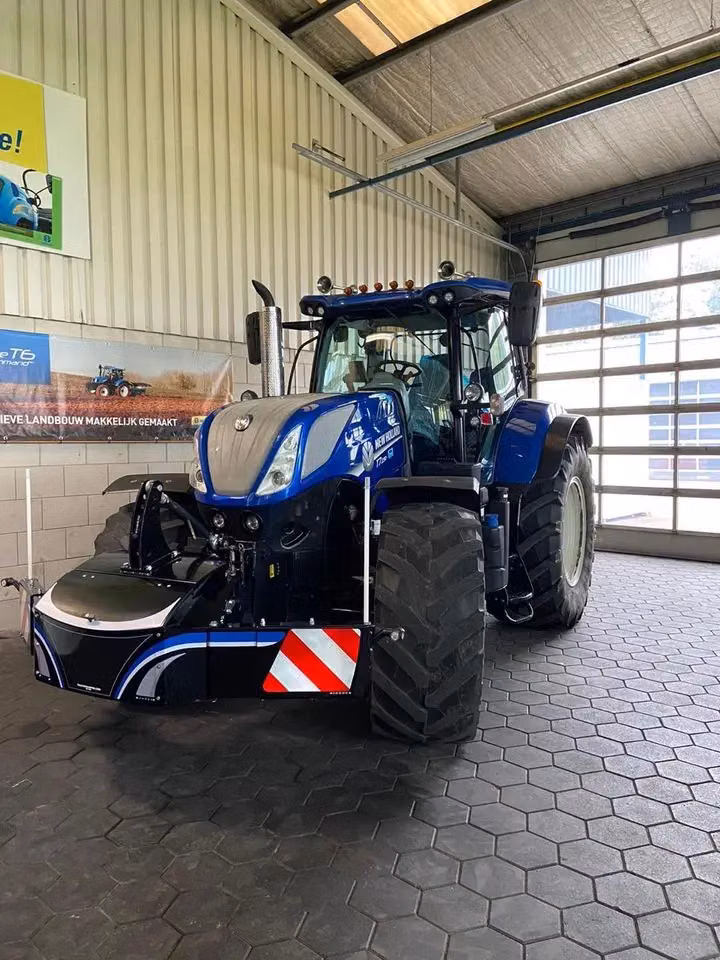 Blue tractor indoors with a black front weight bumper featuring reflective red and white safety stripes