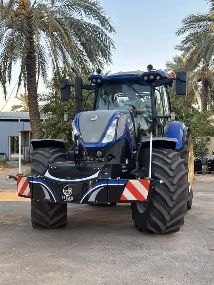 A blue tractor fitted with a large black front weight bumper featuring red and white reflective panels
