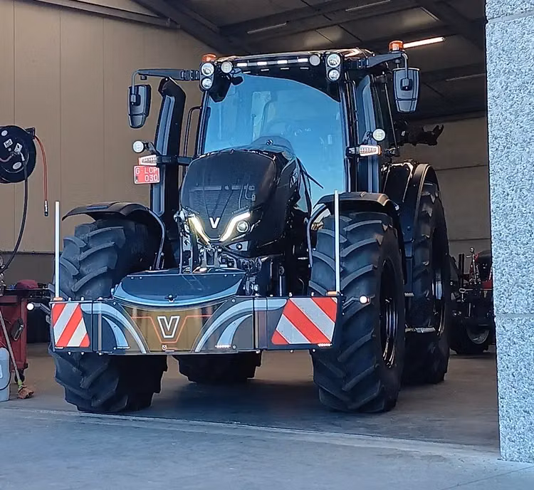 Black tractor in a garage with a metallic front weight bumper featuring red and white warning stripes