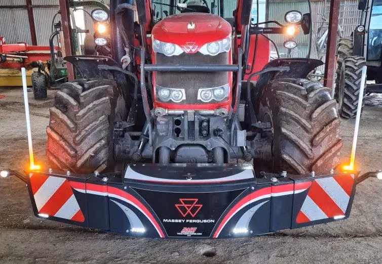 A red Massey Ferguson tractor fitted with a front weight bumper featuring LED lights and safety reflectors