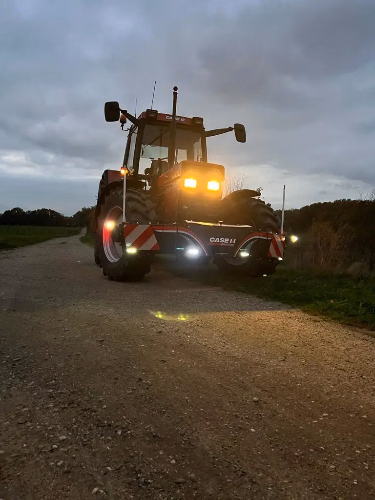 Red tractor with headlights and LED front bumper weight, CASE IH logo visible, parked on a rural dirt road at dusk