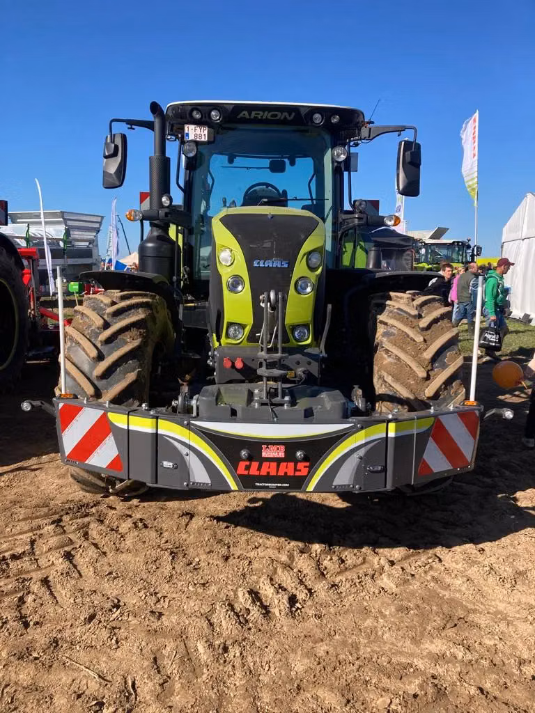 A green tractor fitted with a front weight bumper displaying CLAAS branding and red-white reflective stripes