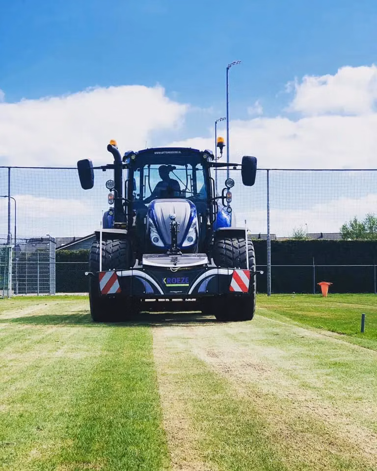 A blue tractor with a front weight bumper and striped safety markings is parked on grass facing forward