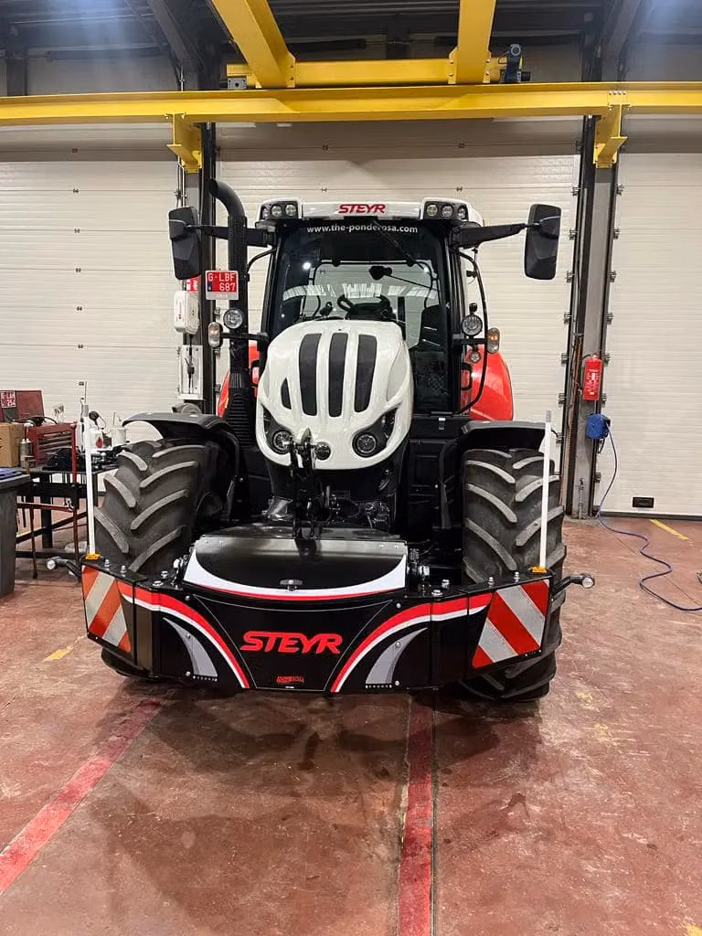 A Steyr tractor indoors with a large black front weight bumper featuring red and white stripes and the Steyr logo