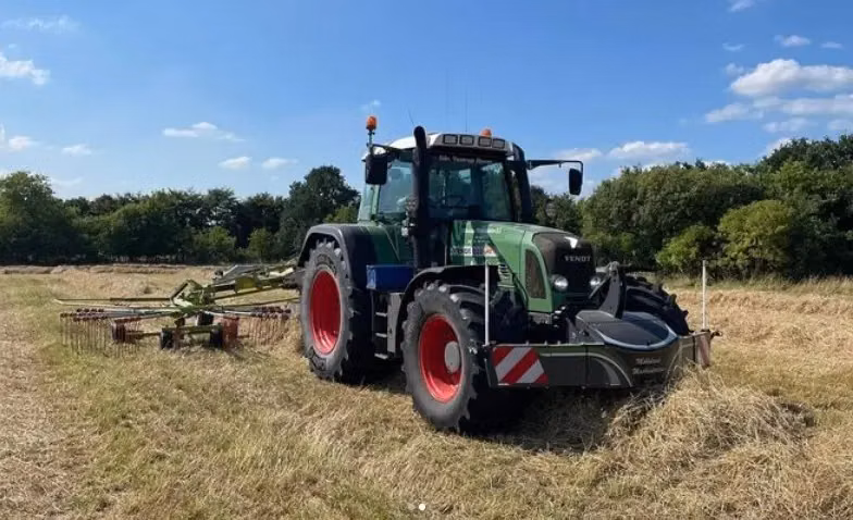 Tractor with red wheels in a field, equipped with a large front weight bumper and farm implement on the back