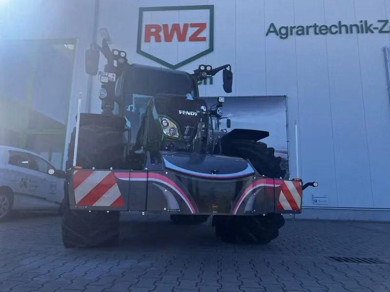 A tractor fitted with a large front weight bumper with red and white reflective stripes, parked outside a building