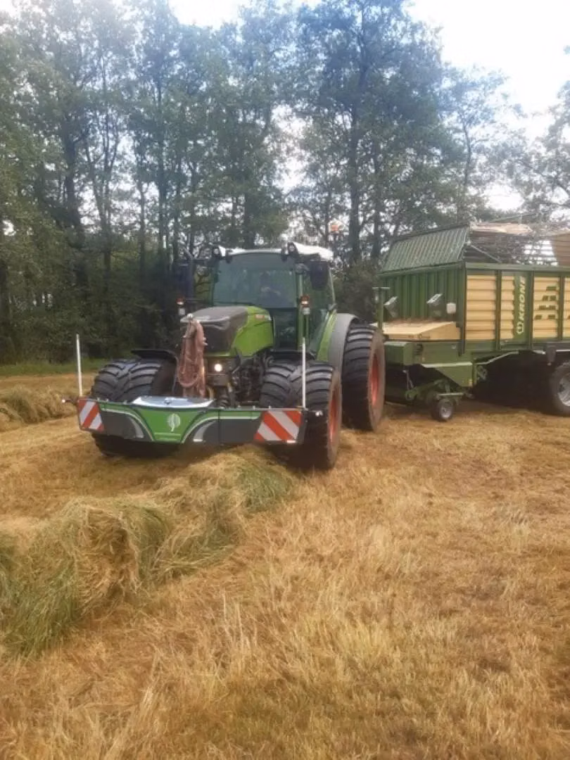 A tractor with a front weight bumper attached, working on a grassy field with a trailer hitched behind