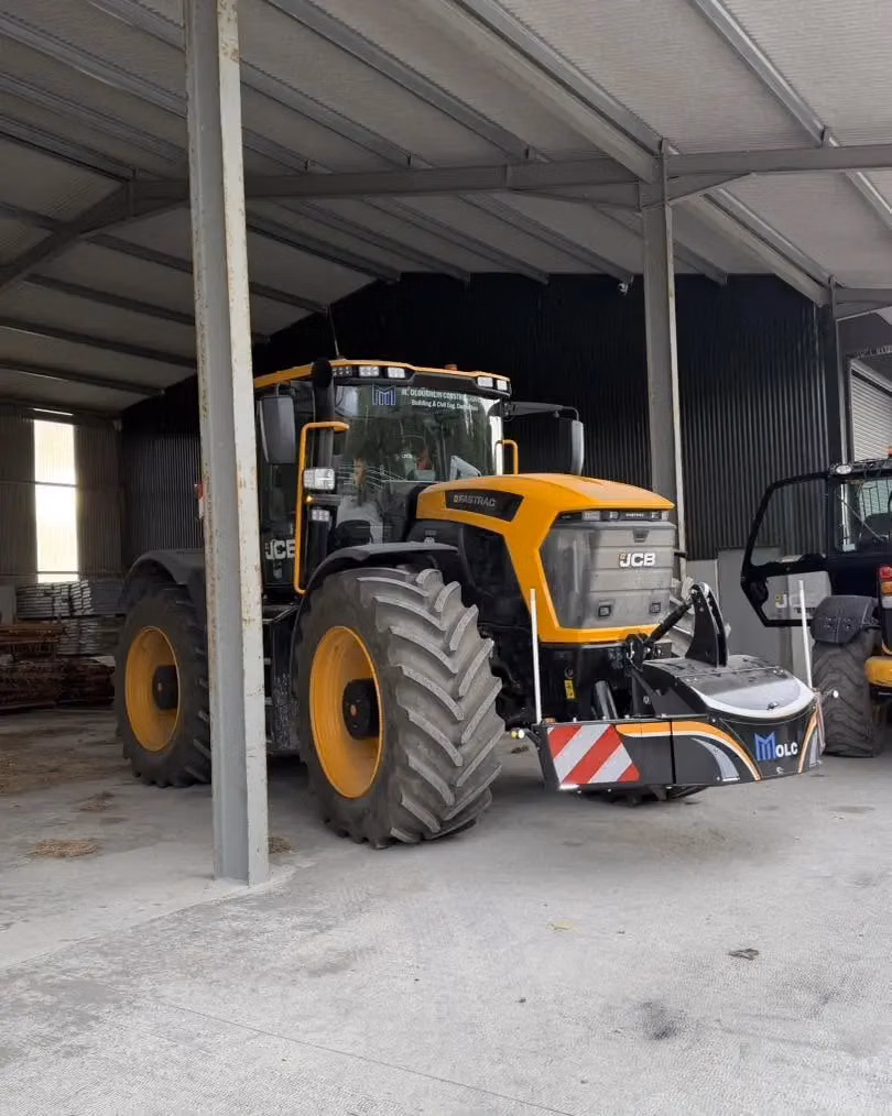 A yellow and black tractor with a front weight bumper featuring reflective red and white stripes parked in a shed