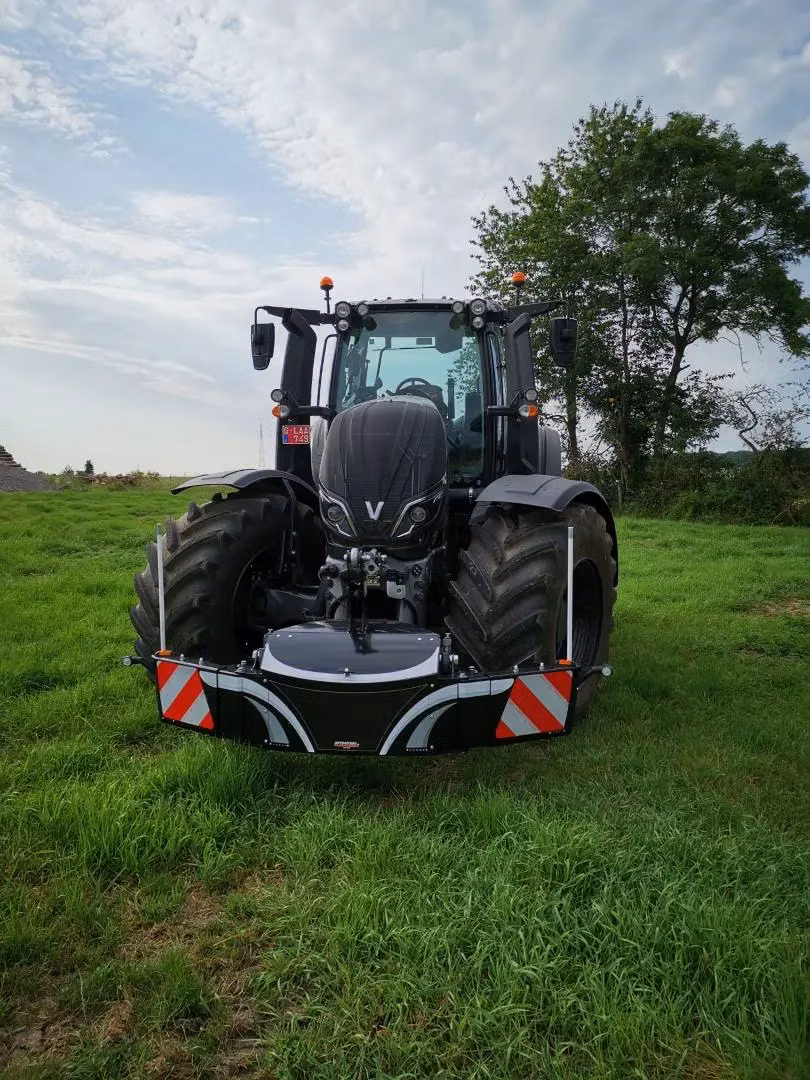 Black tractor on grass fitted with a front weight bumper featuring safety stripes and LED lights