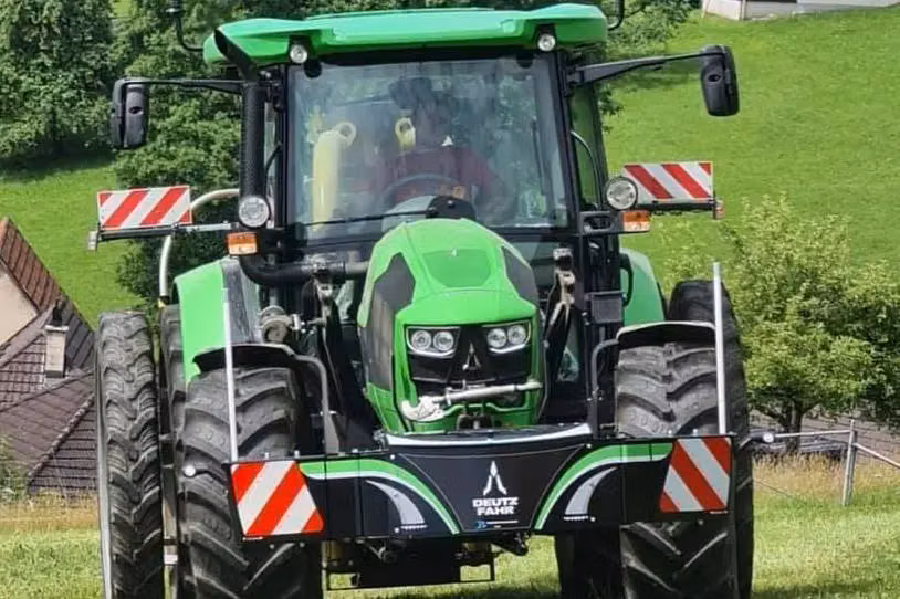 Green tractor with large tires shown from the front, fitted with a Deutz Fahr front weight bumper with hazard stripes