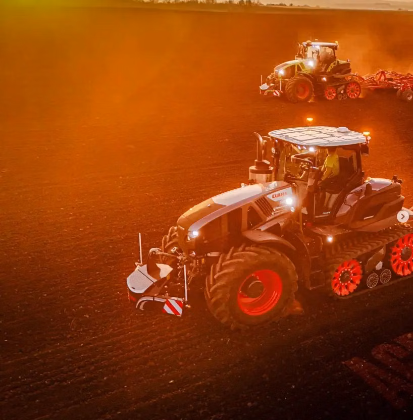 Two tractors with front weight bumpers work on a field at sunset, with one in the foreground and one in the distance