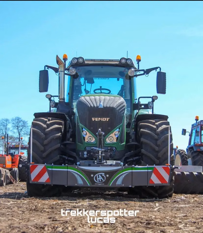 Green tractor with large tires and a front weight bumper featuring reflective red and white stripes in a field